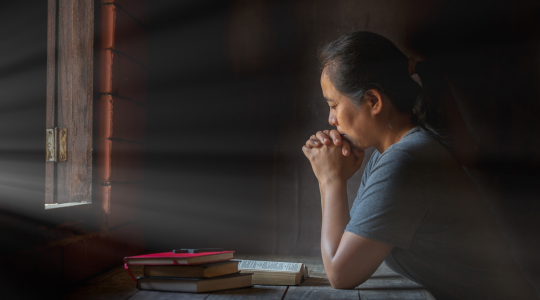 An image of a women praying over a Bible signifying praying and meditation on scripture.